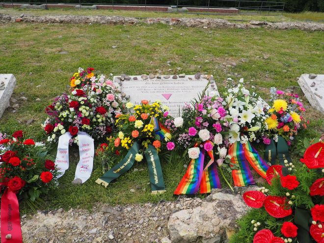 The photo shows various flower arrangements at the memorial stone for the homosexual men imprisoned and murdered by the Nazis in the Buchenwald and Mittelbau-Dora concentration camps. The memorial plaque bears the inscription (in German and English): »In memory of the homosexual men that suffered here / There were 650 Rosa Winkel prisoners in the Buchenwald concentration camp between 1937 – 1945. Many of them lost their lives«.