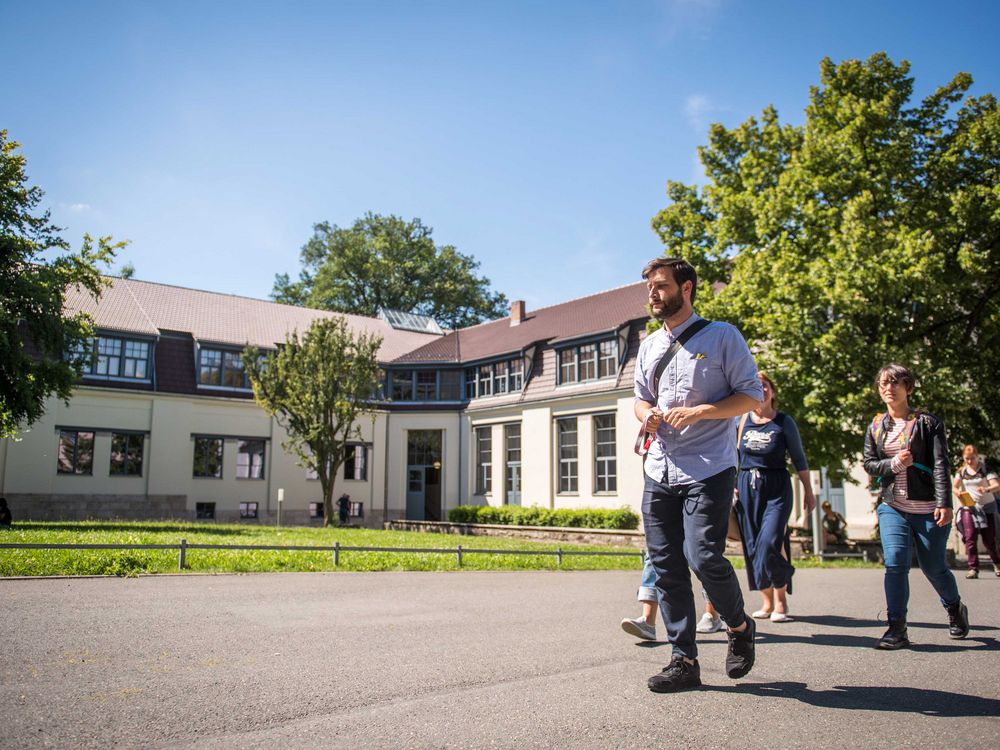 Menschen laufen mit einem Bauhaus.Botschafter vor dem Van-de-Velde-Gebäude entlang