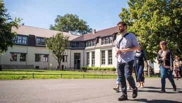 Eine kleine Gruppe Menschen läuft während des Bauhaus-Spaziergangs über den Campus auf das Hauptgebäude zu. Im Hintergrund ist der Van-de-Velde-Bau zu sehen. 