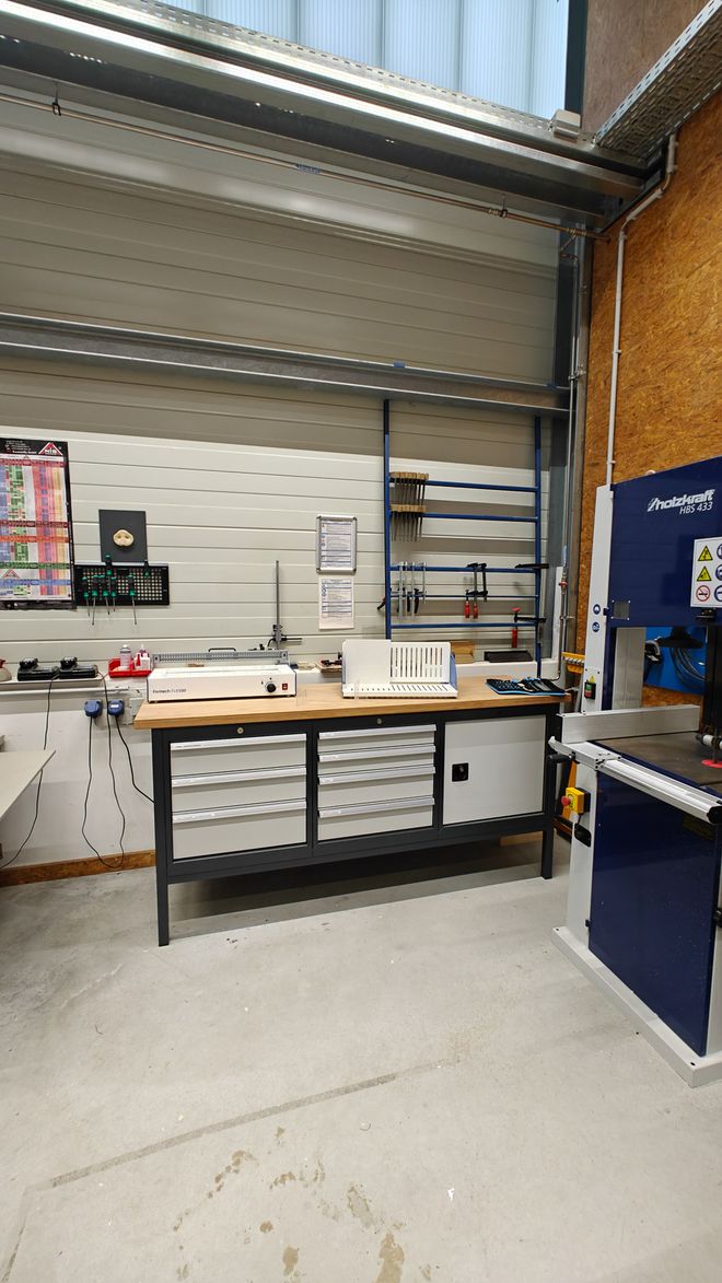 Arbeitsbereich mit Biegewerkzeugen, Werkbank, Schubladenschränken und Werkzeugaufhängungen an der Wand. Der Raum wirkt ordentlich und funktional organisiert.