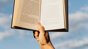 eine Hand hält ein aufgeschlagenes Buch in die Luft