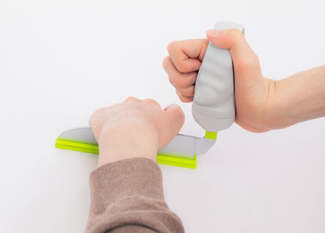 Eine Person verwendet ein Küchenwerkzeug mit breiter Klinge, das an den ergonomisch geformten, individualisierbaren Griff angeschlossen ist; das Werkzeug wird mit einer Hand geführt, während die andere Hand das Arbeitsmaterial stabilisiert.