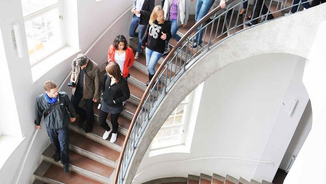 Eine Menschengruppe läuft im Hauptgebäude der Bauhaus-Universität Weimar die Treppe hoch.