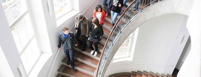 Eine Menschengruppe läuft im Hauptgebäude der Bauhaus-Universität Weimar die Treppe hoch.