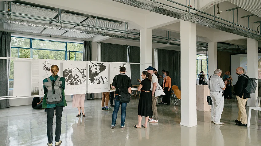 Besuchende in der Ausstellung vor großformatigen Plänen
