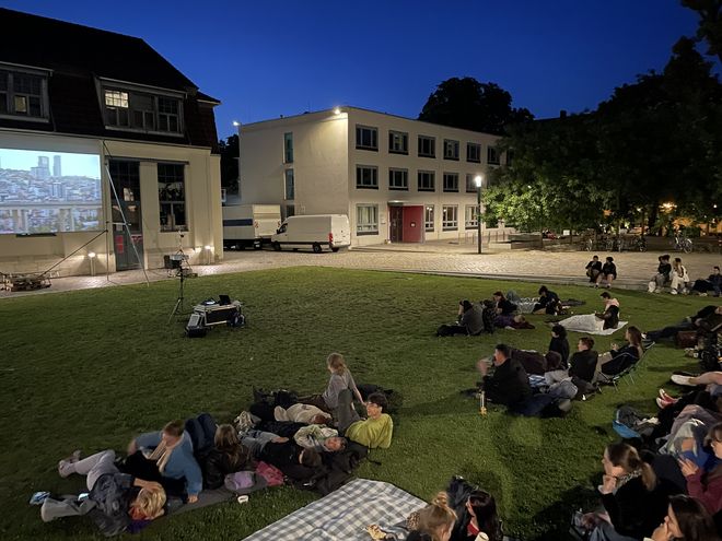 Photo taken during the screening. It shows the guests on the lawn in front of the Van de Velde Building and the screen.