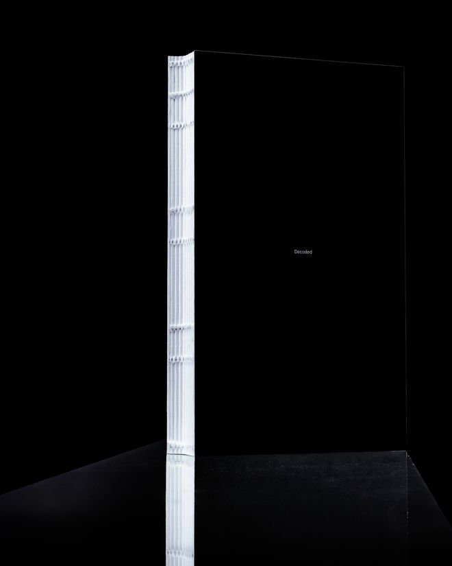 Hochkant stehendes Buch mit schwarzem Cover und weißer offener Fadenheftung, Titel »Decoded« auf der Vorderseite.