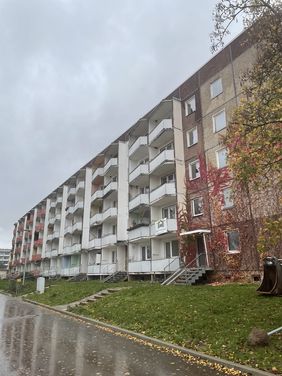 Mehrgeschossiger Wohnblock mit Balkonen an einem regnerischen Tag, Außenansicht eines Plattenbaus