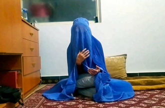 Filmstill: eine verschleierte Frau sitzt auf einem Teppich am Boden
