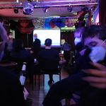 Menschen sitzen in einem dunklen, bunt beleuchteten Raum beisammen