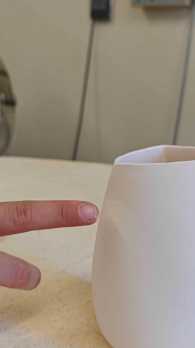 Ein Finger zeigt auf einen Fingerabdruck in der Oberfläche eines weißen keramischen Gefäßes.