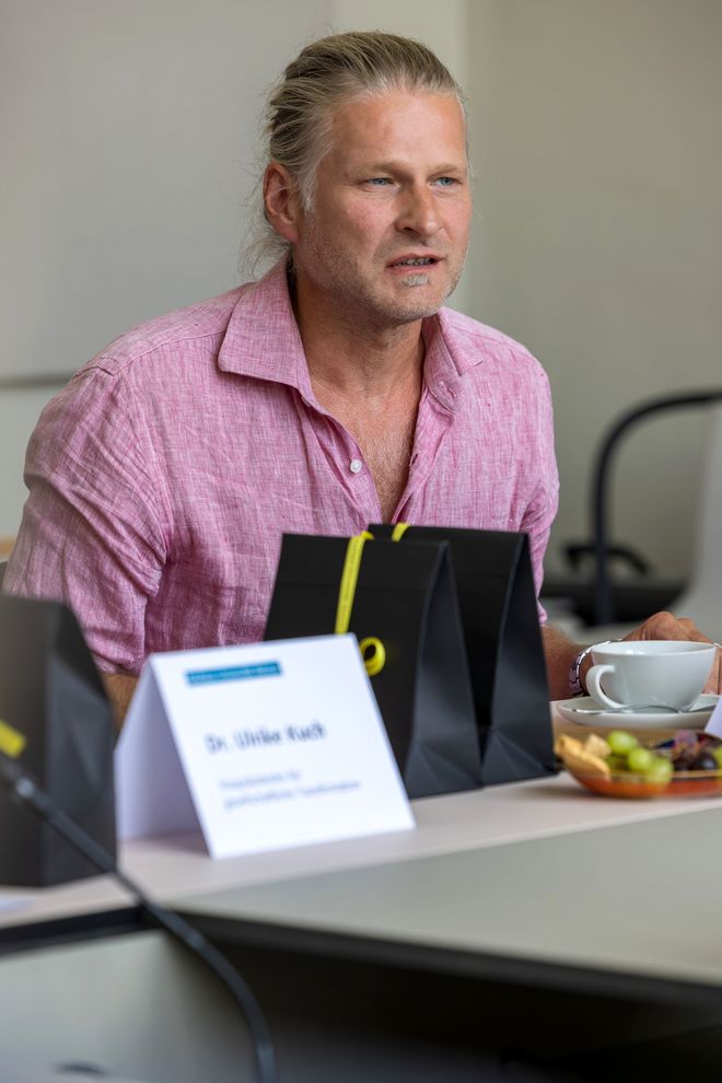 Martin Ahner, wissenschaftlicher Mitarbeiter und Mitglied der Schwerbehindertenvertretung, spricht und sieht konzentriert dabei aus. Er sitzt am Besprechungstisch, vor ihm ein Namensschild von seiner Sitznachbarin sowie kleine Geschenketüten aus schwarzem Papier mit einem gelben Band.