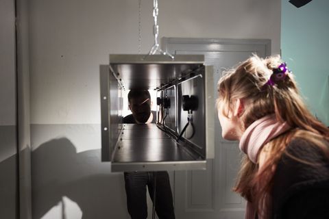 Bauhaus-Universität Weimar bei der Ars Electronica 2026 Eine Frau blickt in eine aufgehängte rechteckige Metallkonstruktion. Auf der gegenüberliegenden Seite ist das Gesicht eines Mannes im Inneren der Konstruktion zu sehen.