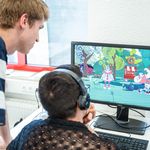 Two people are looking at a screen on which a computer game is running