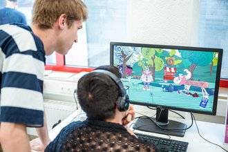 Two people are looking at a screen on which a computer game is running