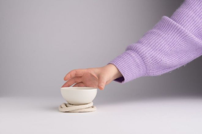 Tasse mit taktiler Struktur steht auf Untersetzer aus Stoff und wird von einer Hand angehoben