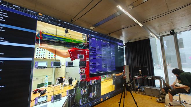 Die Benutzeroberfläche der Software TouchDesigner ist auf einer großformatigen LED-Wand geöffnet. Im Hintergrund ist ein Kamerabild mit digitalen Effekten zu sehen