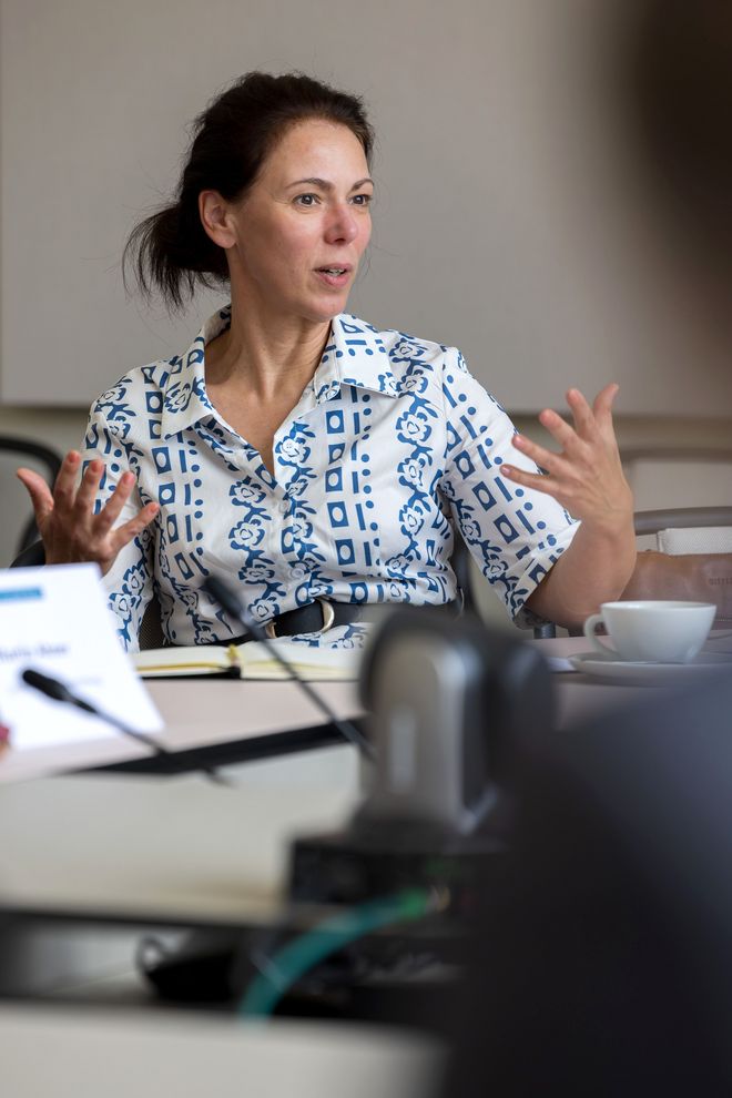 Pressesprecherin Claudia Weinreich am Besprechungstisch: Sie spricht und gestikuliert mit beiden Händen, dabei sieht sie konzentriert aus.