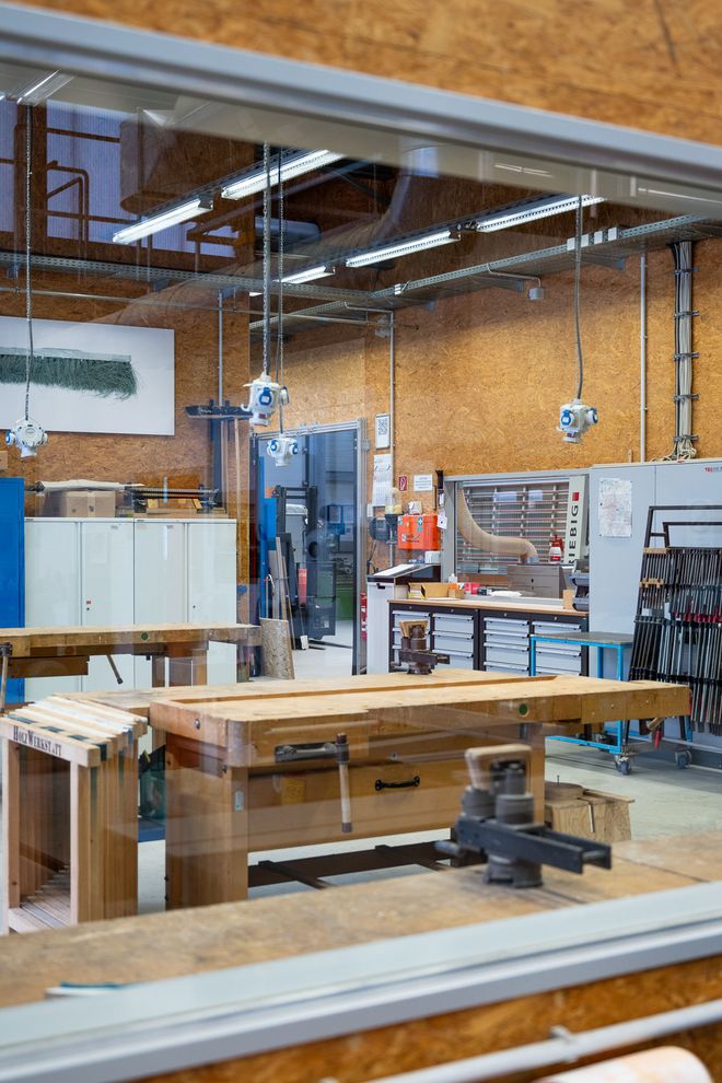 Workshop view with several woodworking machines, workbenches, and stored wooden strips. The space is bright and technically equipped.