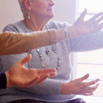 eine ältere Frau bewegt sich sitzend, die Arme erhoben