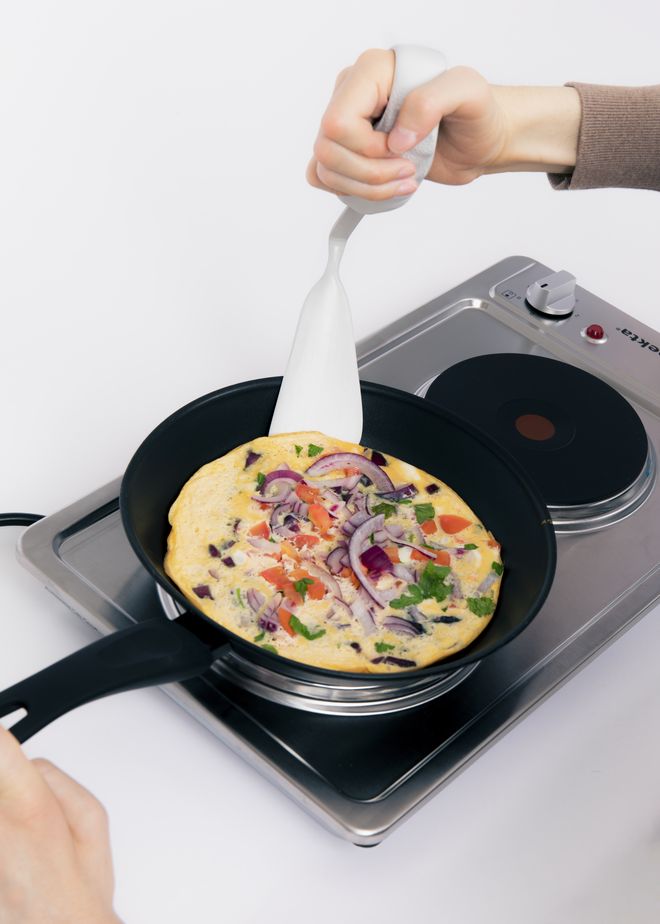 Eine Person mit Cook Ability Griff und Pfannenwenderaufsatz kocht Omelett in einer Pfanne