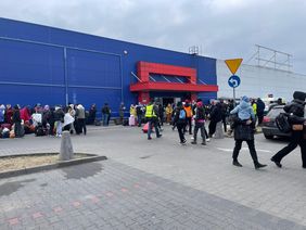 Menschen mit Kindern auf den Armen vor einem Logistikzentrum.