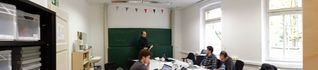 project group in lab around table with teacher infront of blackboard, left a cubboard with boxes 
