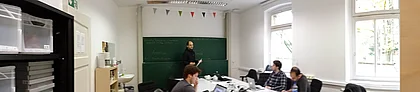 project group in lab around table with teacher infront of blackboard, left a cubboard with boxes 