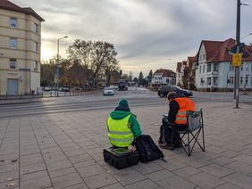 Zwei Männer sitzen auf Campingstühlen und tragen Daten in Tabellen auf Klemmbrettern ein