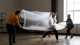 Drei Studierende tanzen, während sich eine Person unter einer sich wölbenden, halb-transparenten Folie befindet