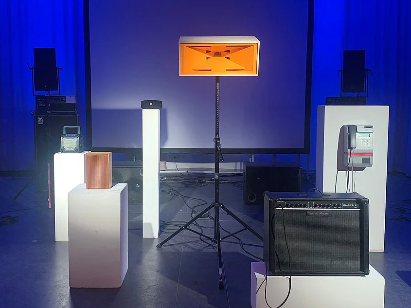 Blue-lit room of the Studio for Electroacoustic Music (SeaM) with loudspeakers, amplifiers and other audio equipment displayed on white plinths.