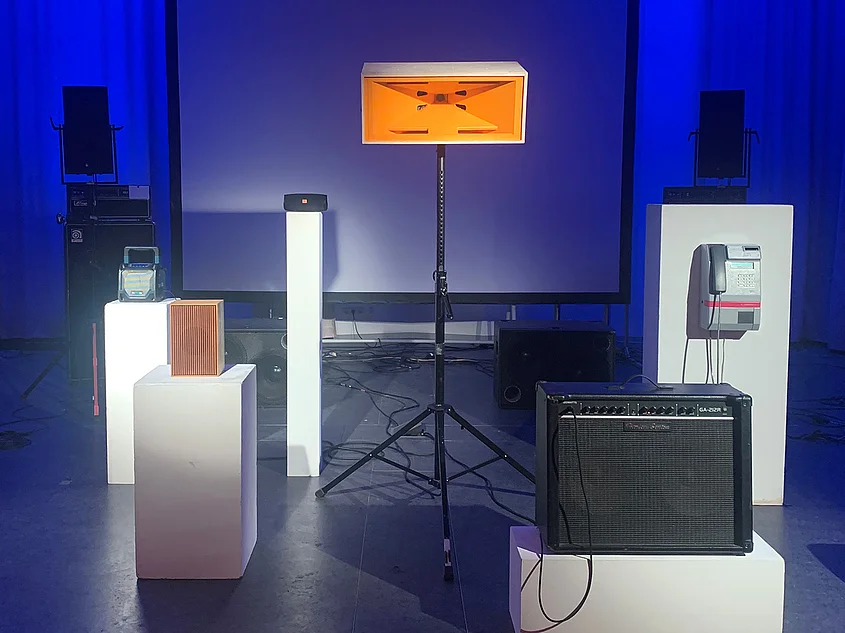 Blau beleuchteter Raum des Studios für elektroakustische Musik (SeaM) mit Lautsprechern, Verstärkern und weiteren Audiogeräten auf weißen Sockeln.