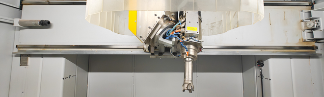 Detailansicht des Fräskopfes einer CNC-Maschine mit eingesetztem Werkzeug, umgeben von einer transparenten Schutzabdeckung im Innenraum der Maschine.