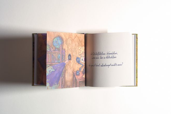 Open picture book with a colourful interior illustration on the left and handwritten text on the right.