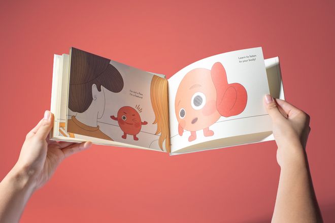 Book view of »RED AF* – Red Asian Flush« by Soo Ah Youn and Anastasia Fast: two hands hold an open illustrated book against a red background. The pages show the character »Blush« and a message about listening to one’s body.