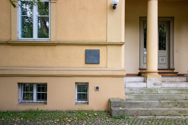 [Translate to English:] Ansicht einer Eingangssituation eines Hauses. Links der durch eine Stütze gegliederten Eingangssituation befindet sich eine Bronzetafel mit der Inschrift: Ghettohaus 1940 – 1942 1900 Wohnhaus des Ehepaares Friedrich Fleischer, Kunstschulprofessor Jenny-Fleischer-Alt, Kammersängerin 1940/41 Zwangseinweisung jüdischer Bürger Zum Gedenken an: Jenny Fleischer-Alt Freitod 1942 Edith Gál Freitod 1942 Ilka Gál Tod 1942 Käthe Friedländer Deportation 1942 verschollen Martha Kreiss Tod 1944 Eduard Rosé, Deportation 1942 Cellist, Konzertmeister Tod 1943 in Theresienstadt