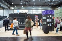 Fair view of »Ein Messestand für Leipzig«: visitors move in front of the Faculty of Art and Design’s stand, designed as an underground station entrance. Another presentation stand with publications is visible on the right.