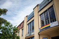 The photo shows a banner with the »Intersex-Inclusive Progress Pride Flag« hanging from the balcony of the Main Building of the Bauhaus-Universität Weimar.