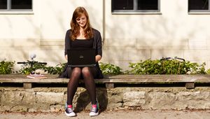 Person mit Laptop draußen vor einem Uni-Gebäude