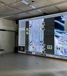 Eine Videoleinwand, auf der Visualisierungen und Tabellen mit Parametern zu sehen sind. 