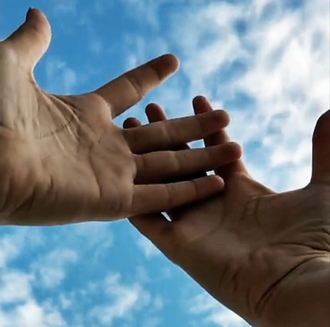 Filmstill: Zwei Hände berühren sich vor einem Himmel