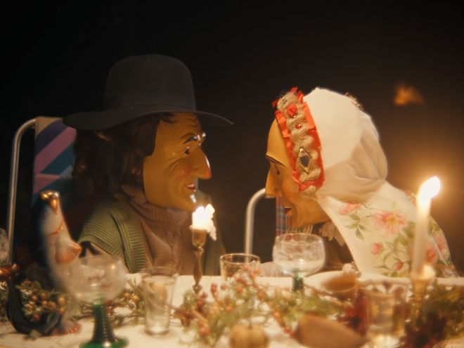 Zwei Personen sitzen sich an einem Tisch mit Kerzen und Geschirr gegenüber.