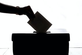 Eine Hand wirft einen Wahlzettel in eine Wahlurne ein.