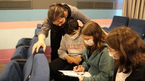 Drei Schlüer*innen beugen sich über ein Dokument, in welchem sie intensiv lesen. Foto: Bauhaus-Universität Weimar, Serap Resimcioğlu