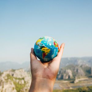 Hand holding a globe in front of a blurred landscape