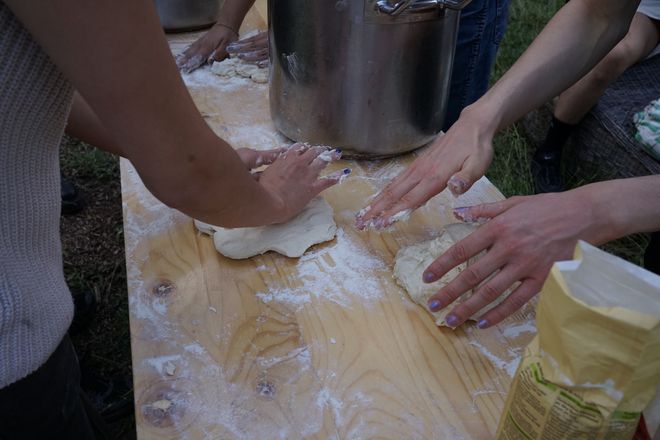 Three pairs of hands kneading pizza dough on a wooden table.