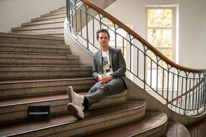 Moderator Jo Schück sitzt auf der Treppe im Hauptgebäude der Universität.