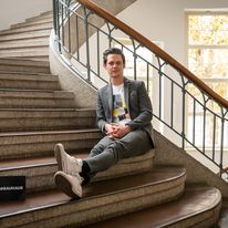 Moderator Jo Schück sitzt auf der Treppe im Hauptgebäude der Universität.