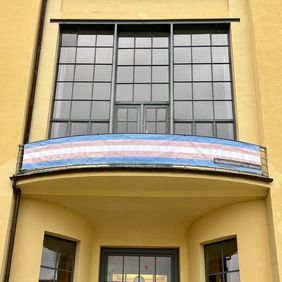 Banner in the colors of the Trans Pride flag on the balcony of the Main Building.