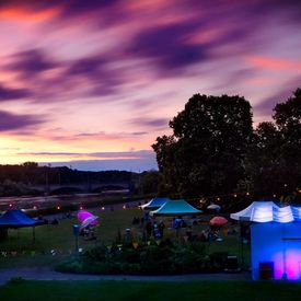 Szene vom Hörspielsommer: Wiese mit Zelten, bunten Schirmen und Menschen im Abendrot; Foto: Tino Pfund